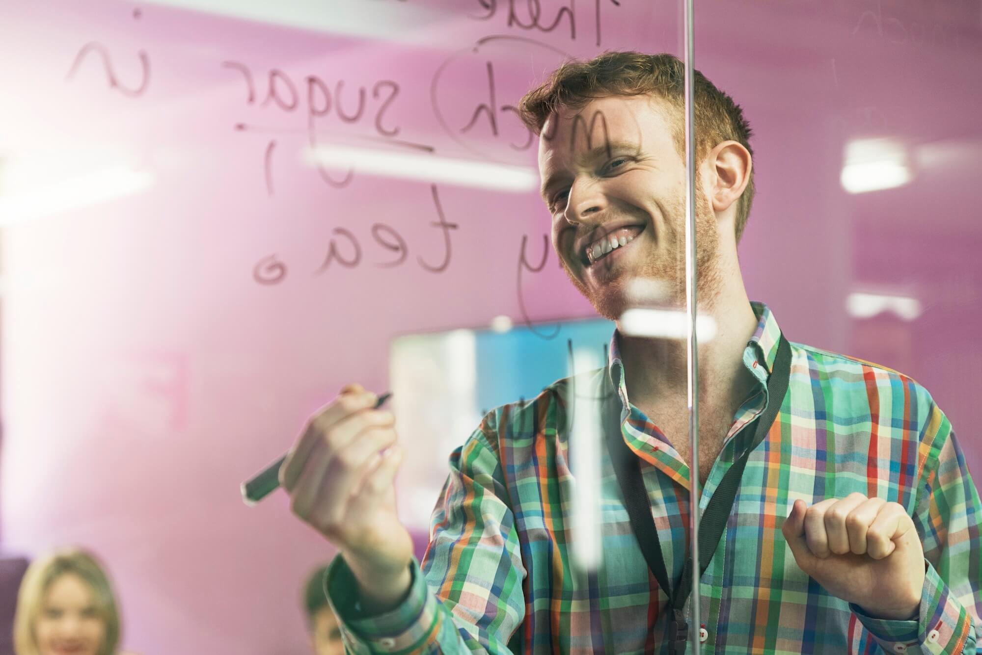 A smiling presenter writing on a transparent board during a team session